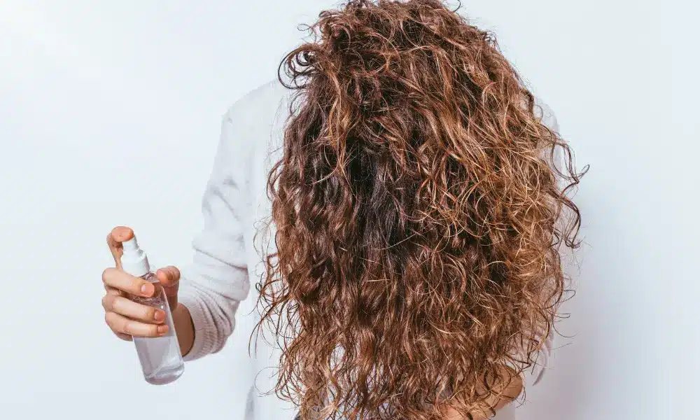 a girl spraying liquid in her curly hair